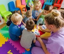 Young children sitting in a circle on a colorful play mat with their teacher